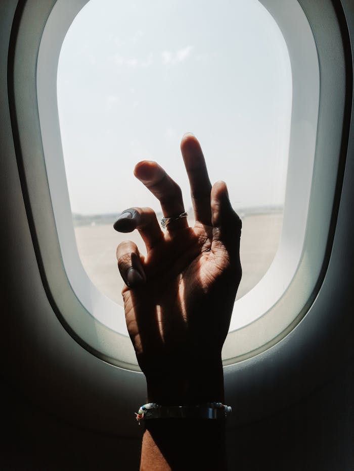 services-03 A person's hand gestures against an airplane window, highlighting in-flight aesthetics.